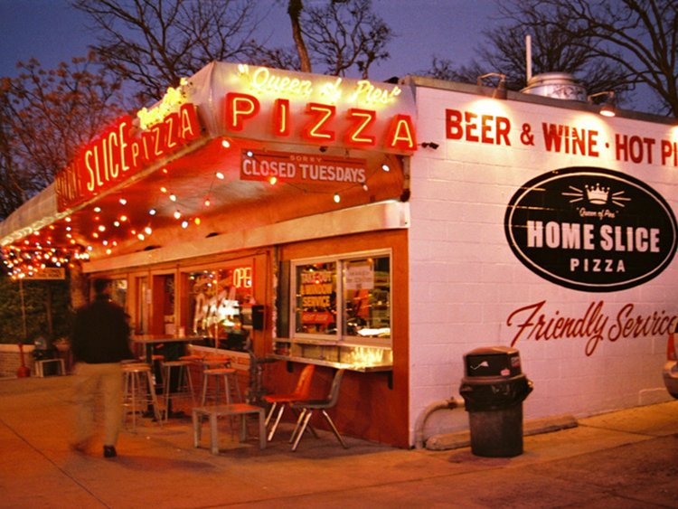 Home Slice Pizza"s Christmas lights light up outdoor dining. Sign says, "Queen of Pies."