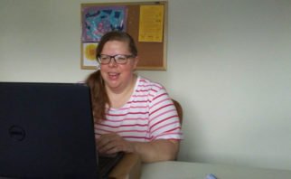 Writer sitting at desk working on laptop and smiling.