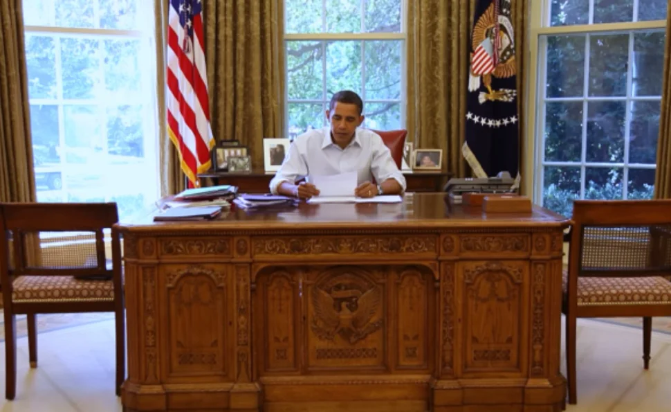 Former President Barack Obama is sitting behind his desk in the Oval Office.