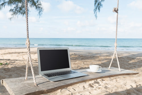 Laptop and cup of coffee with the beach in the background.