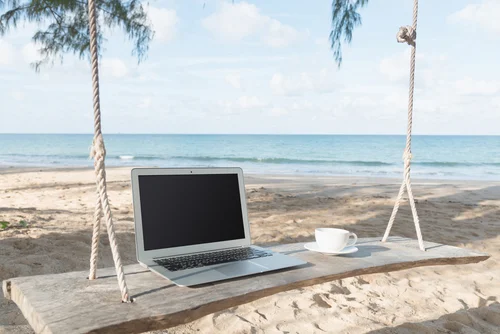 Laptop and cup of coffee with the beach in the background.